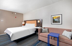 Hotelkamer met een bed, een slaapbank, een kleine tafel, een wandlamp, een schilderij en een thermostaat.