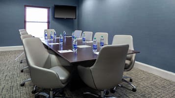 Une salle de conférence avec une longue table, six chaises, des bouteilles d’eau et un téléviseur à écran plat fixé au mur.