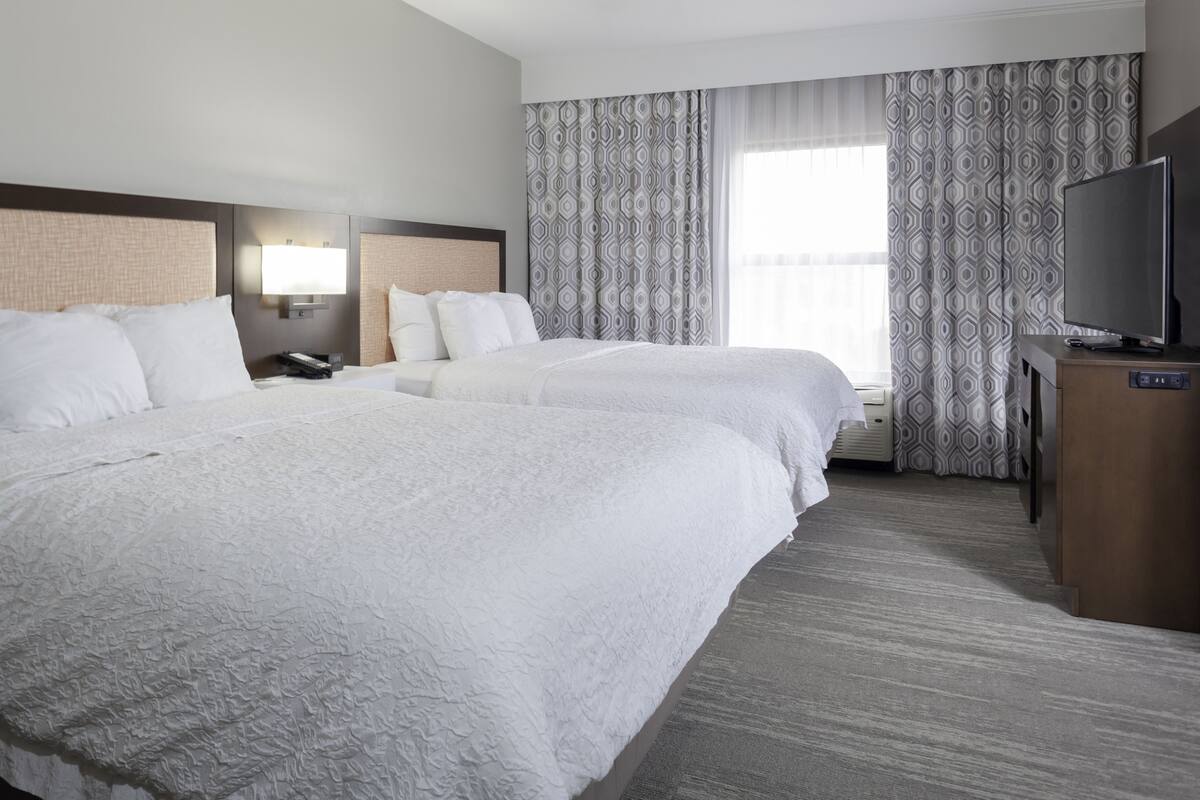 A hotel room with two beds, a television, and a desk.