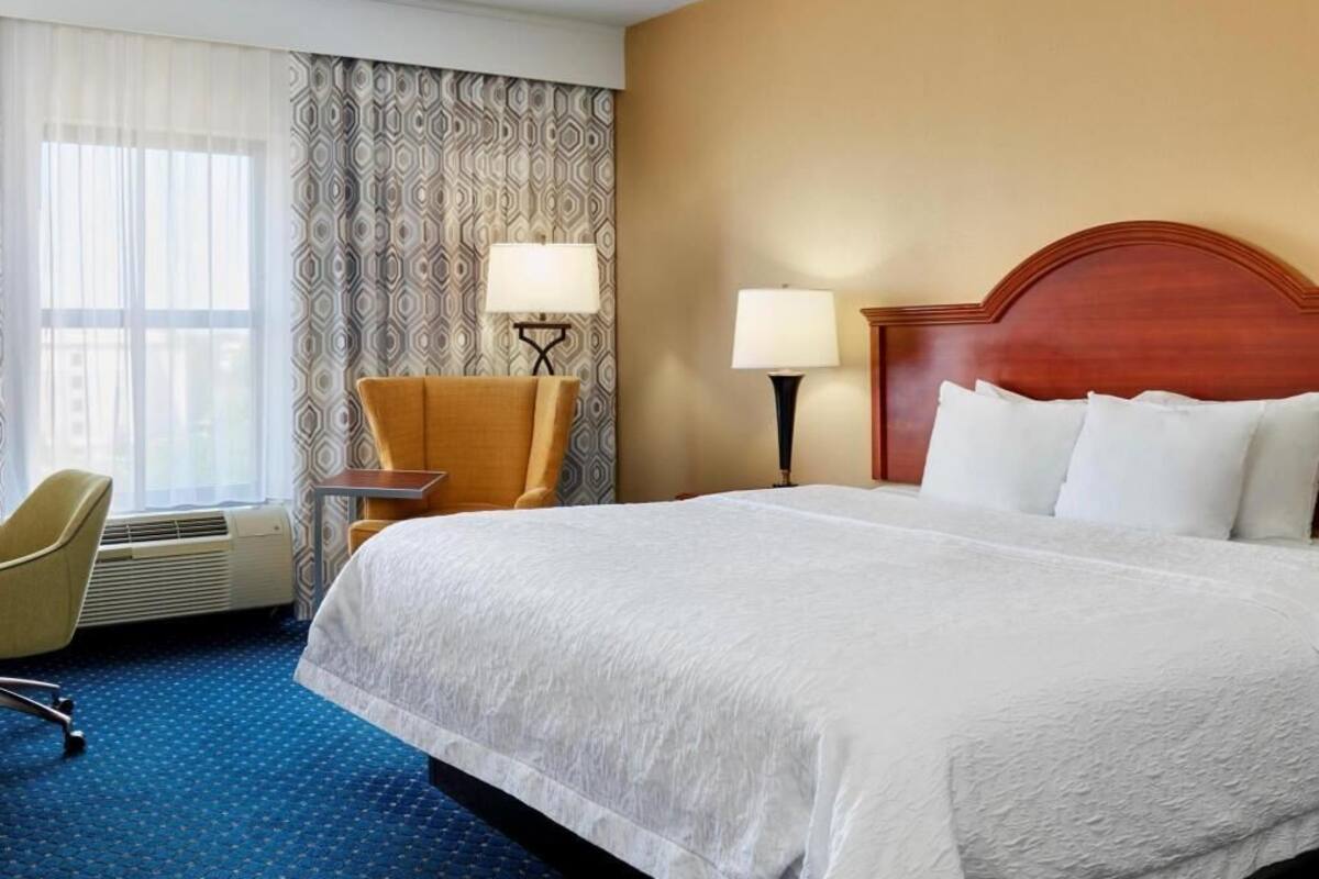 A hotel room with a large bed, a desk, a chair, and a window with curtains.