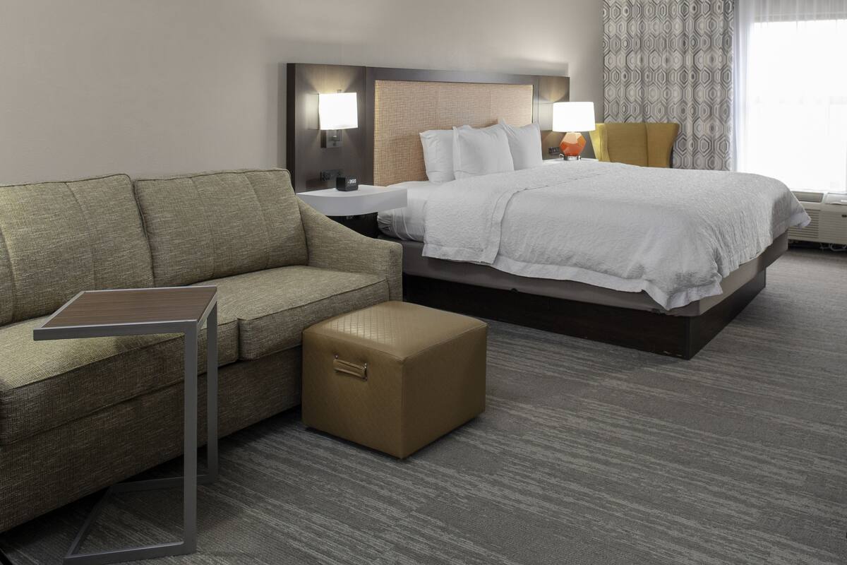 A hotel room with a bed, a sofa, a small table, and a nightstand.