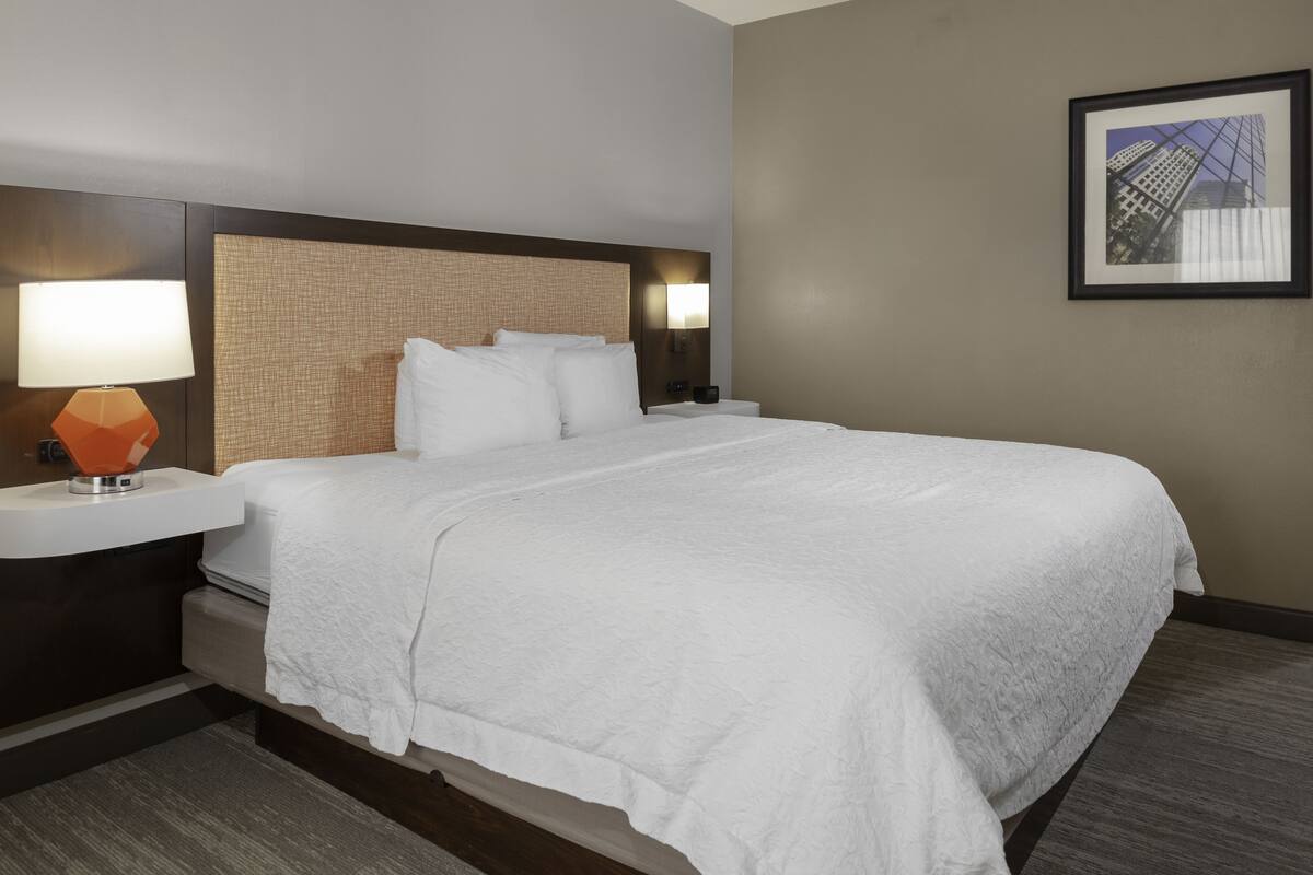 A hotel room with a large bed, a nightstand with a lamp, and a framed picture on the wall.