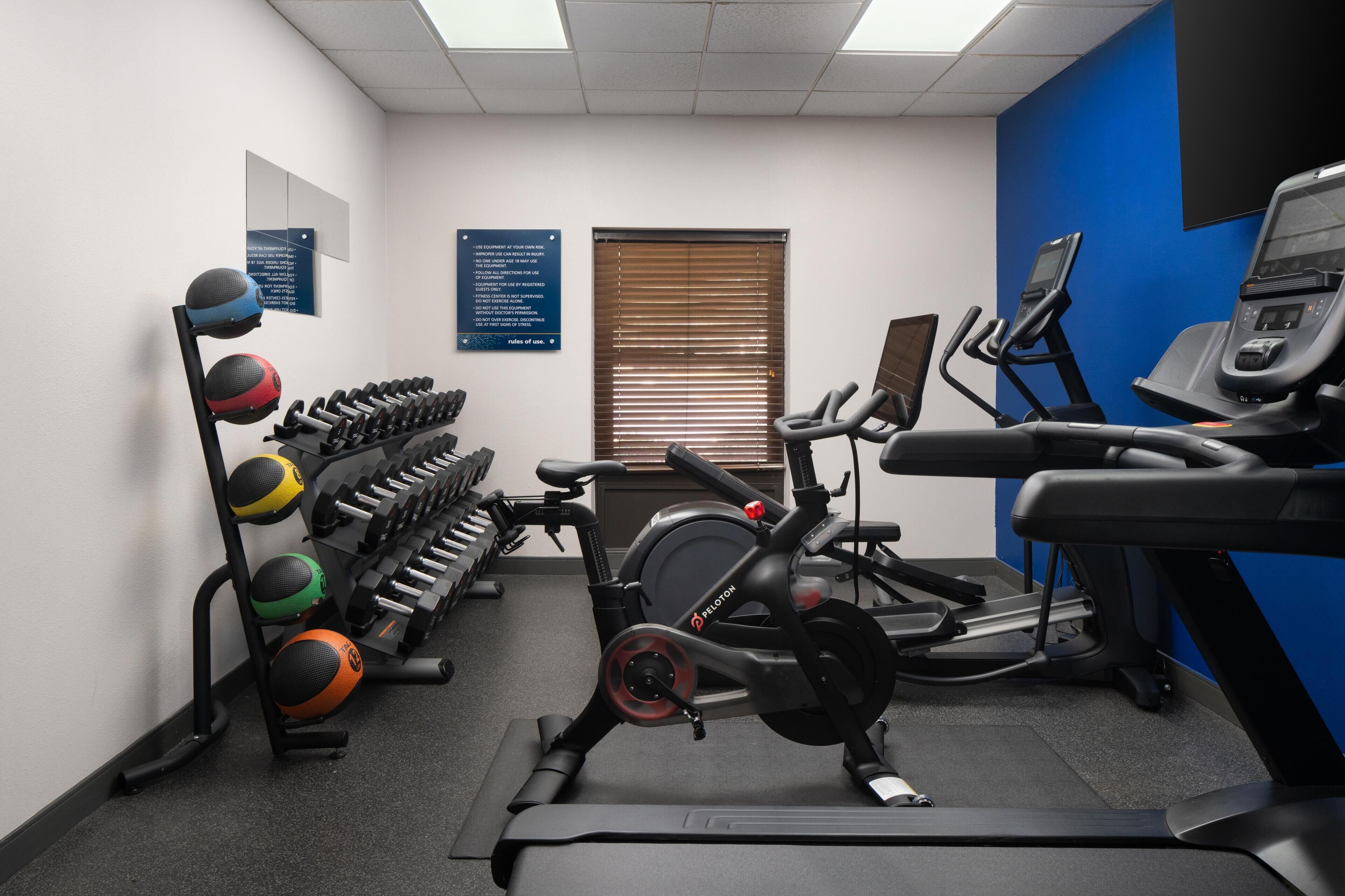 Un gimnasio con equipamiento de ejercicio, que incluye una cinta de correr, una bicicleta estática y varios pesas.