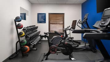Un gimnasio con equipamiento de ejercicio, que incluye una cinta de correr, una bicicleta estática y varios pesas.