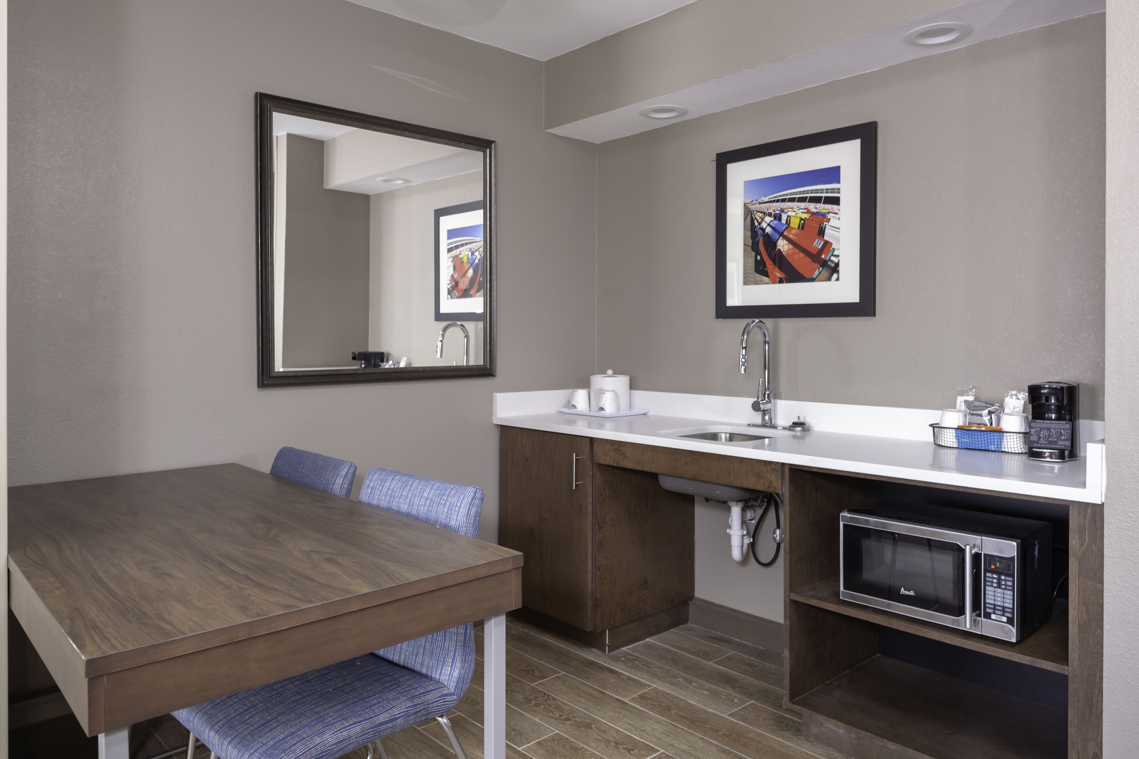 Een compacte hotelkamer met een houten eettafel, een inbouwmagnetron, een wastafel en een grote spiegel.