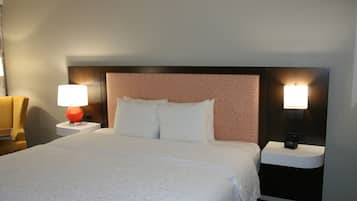 A hotel room with a large bed, two bedside tables, a red lamp, and a nightstand with a clock.
