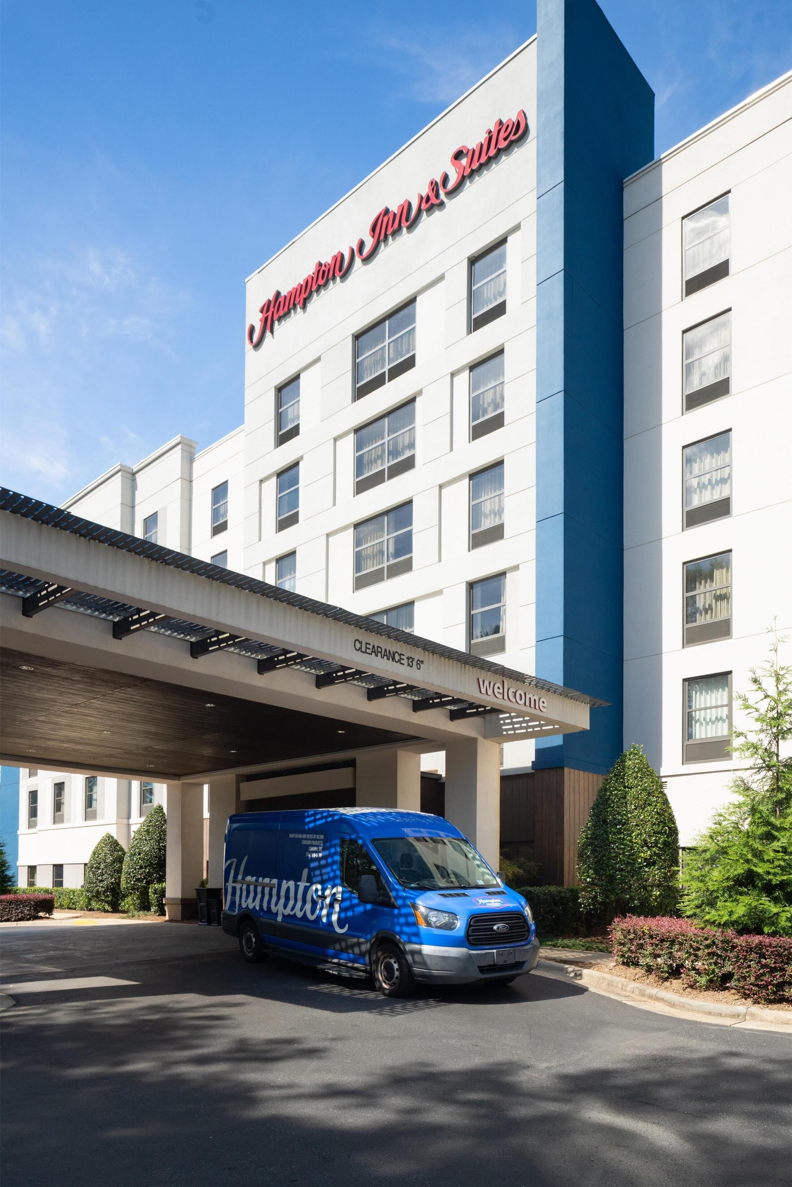 Edifício do Hampton Inn & Suites com uma van azul estacionada em frente.