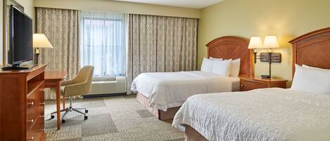 A hotel room with two beds, a desk with a television, a chair, and a desk lamp.