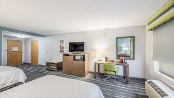 Una habitación de hotel con dos camas, un escritorio con computadora, un televisor, un espejo y una ventana.