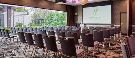 A conference room with rows of chairs, a large screen displaying 'Holiday Inn', and a projector.