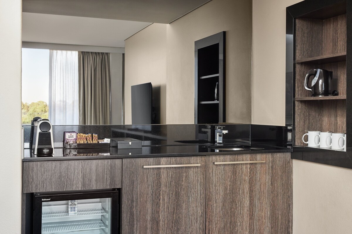 A modern kitchen with a black countertop, wooden cabinets, a coffee machine, and a coffee maker.
