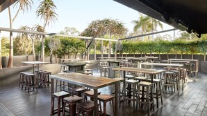 An outdoor dining area with multiple tables and stools, surrounded by greenery and trees. - Holiday Inn Warwick Farm by IHG (Cabramatta)