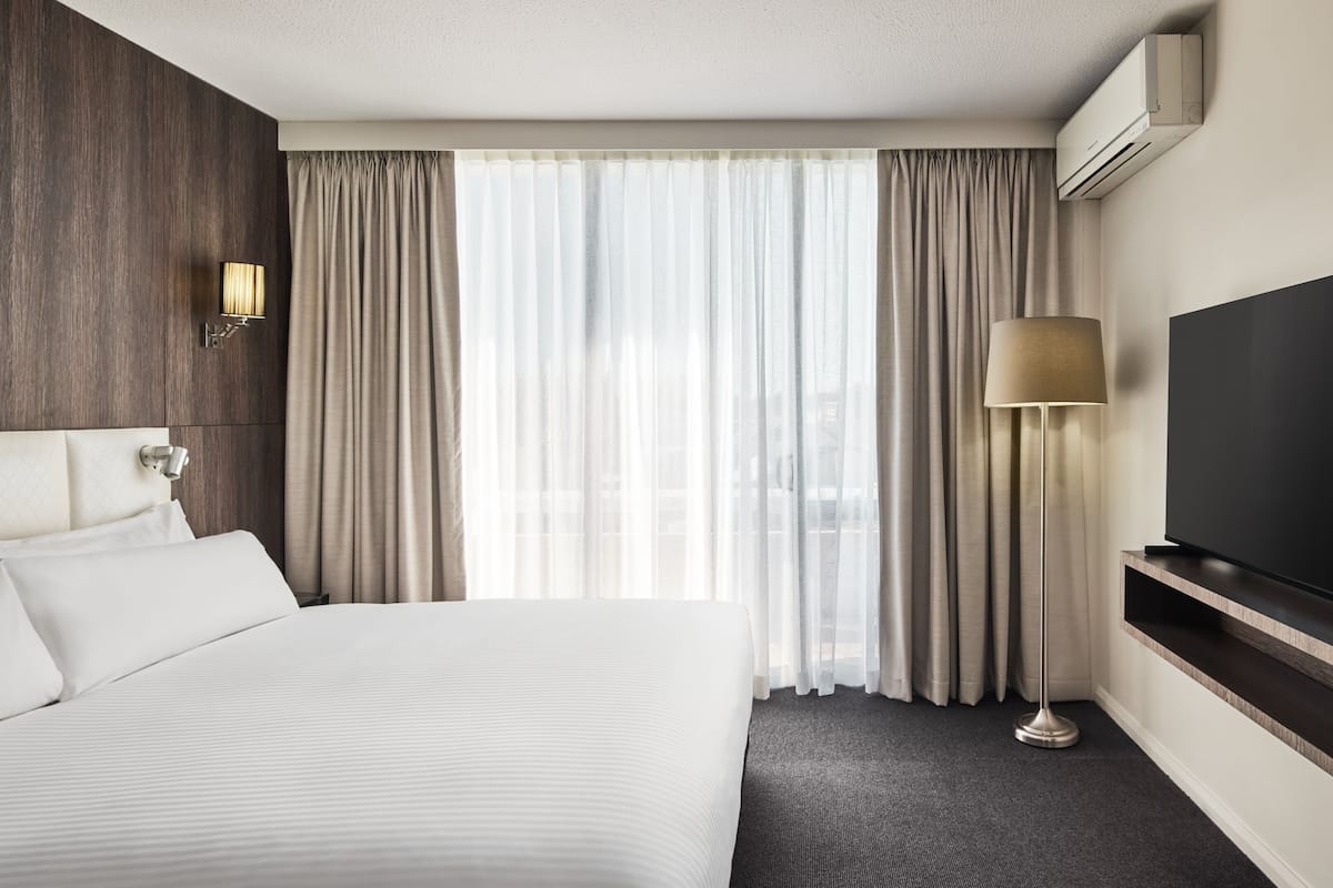 A hotel room with a large bed, a flat-screen TV, a lamp, and a window with curtains.