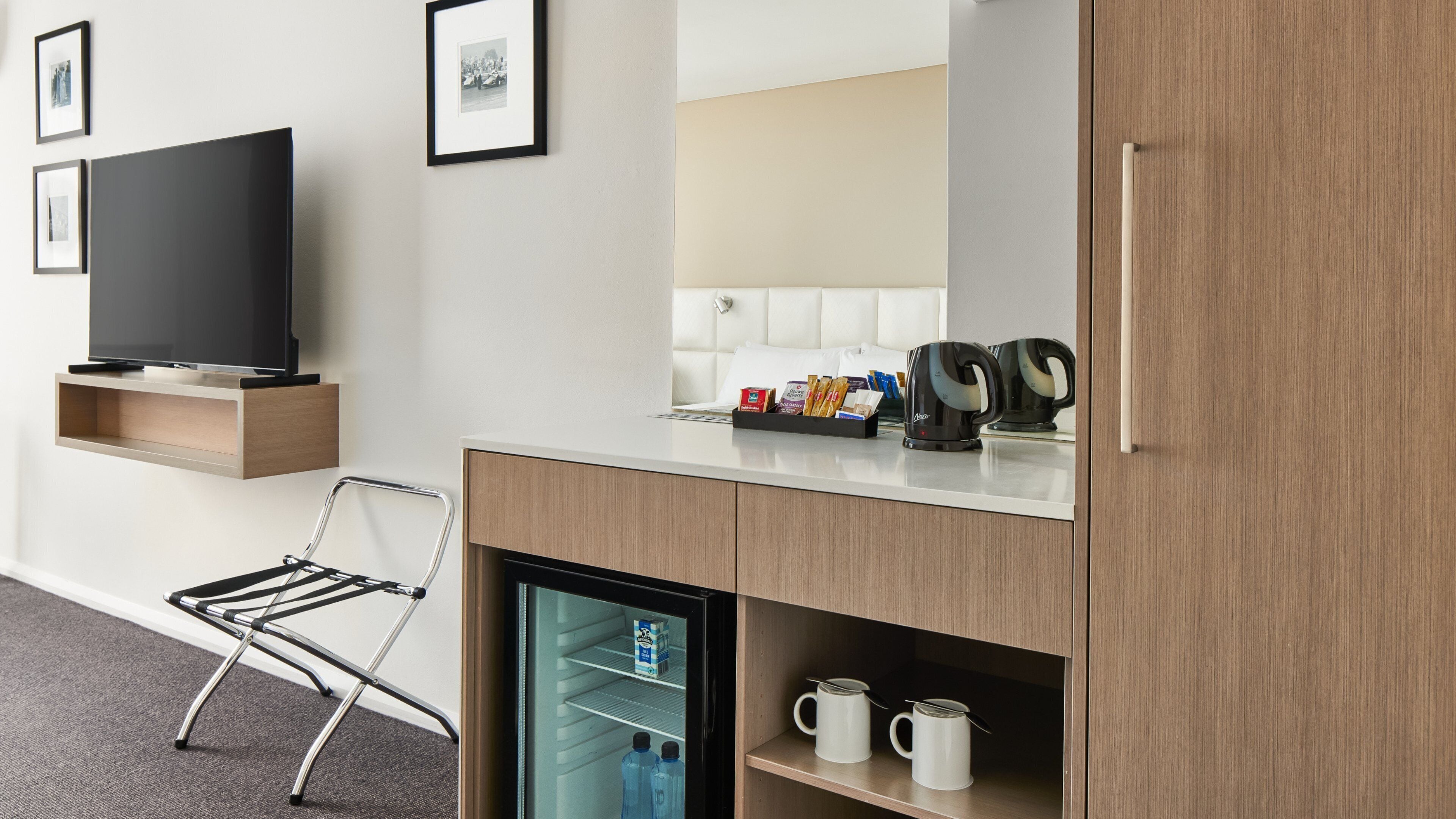 A hotel room with a flat-screen TV, a foldable chair, a minibar, a coffee maker, and a refrigerator.