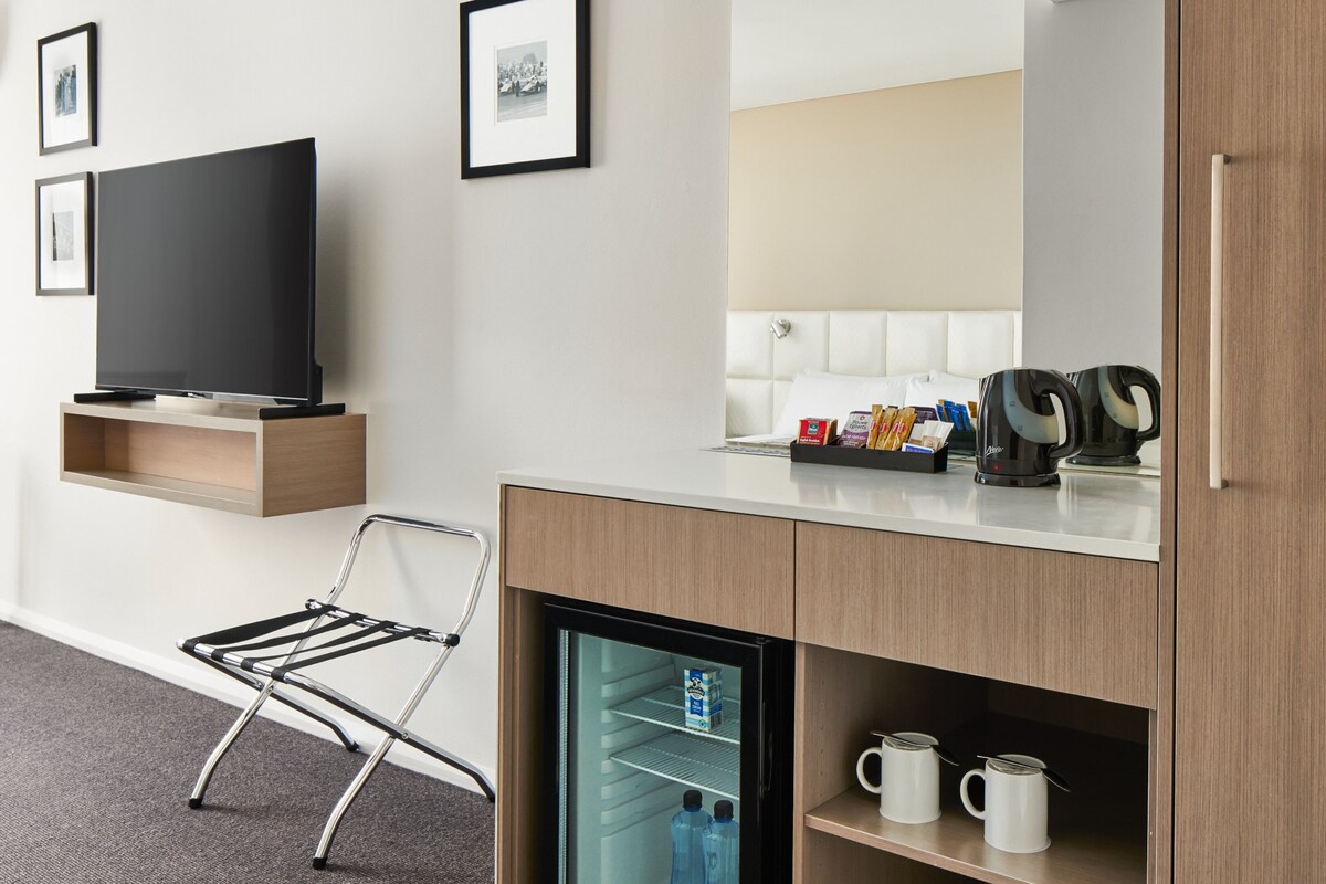 A hotel room with a flat-screen TV, a foldable chair, a minibar, a coffee maker, and a refrigerator.