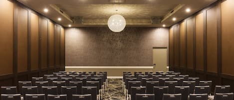 Un salón de conferencias con filas de sillas, una alfombra estampada y una gran lámpara de araña.