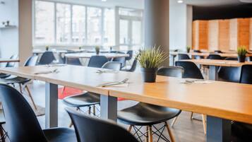 Un espace de restauration moderne avec de longues tables, des chaises noires et des plantes en pot.