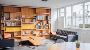 Uma sala de estar moderna com uma grande estante de madeira, um sofá de couro, uma mesa redonda de madeira e vista para a rua através de amplas janelas.