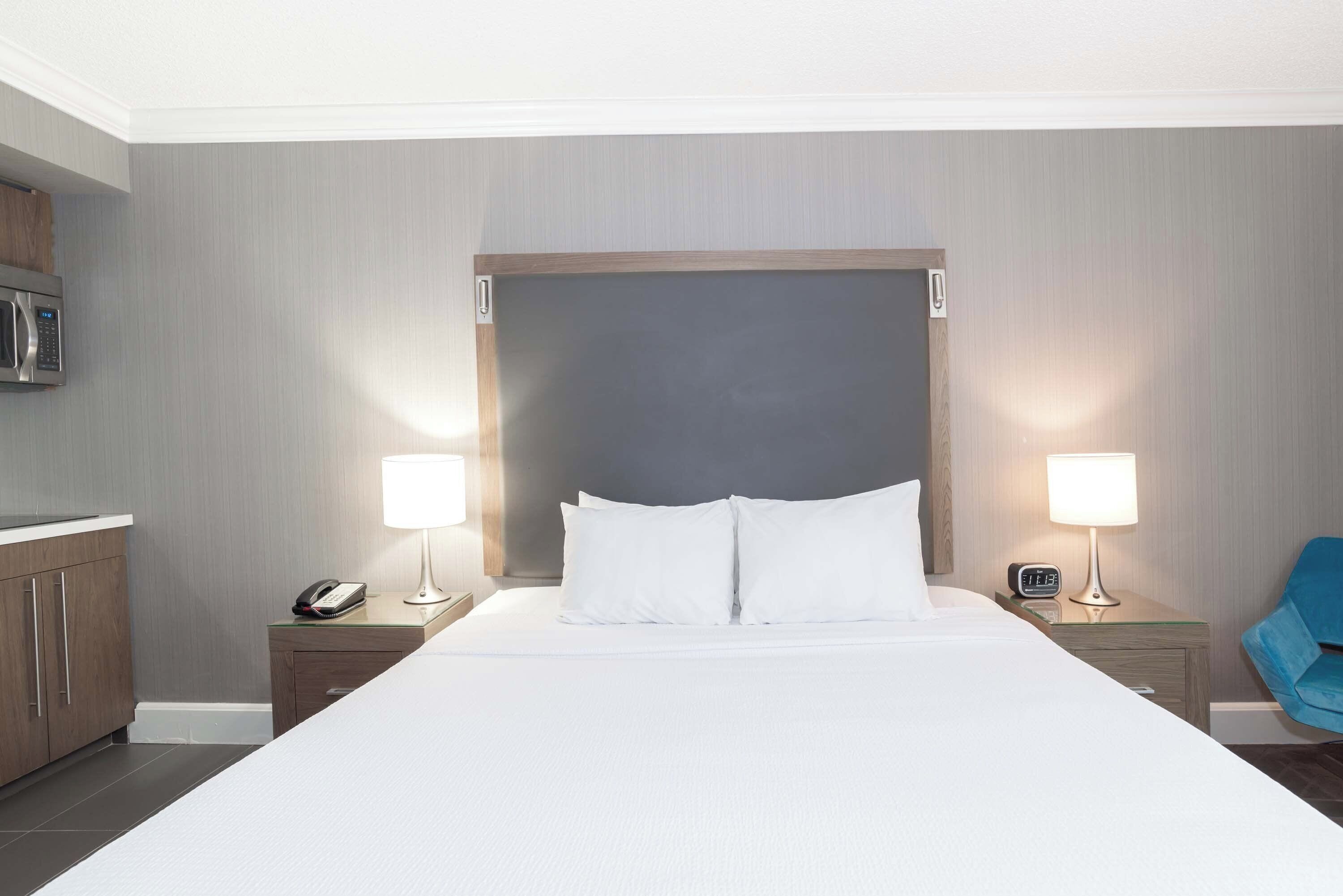 A hotel room with a large bed, two bedside tables with lamps, a microwave, and a blue chair.