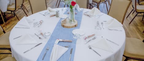Een ronde eettafel, gedekt met witte tafelkleden, een blauwe loper en witte servetten.