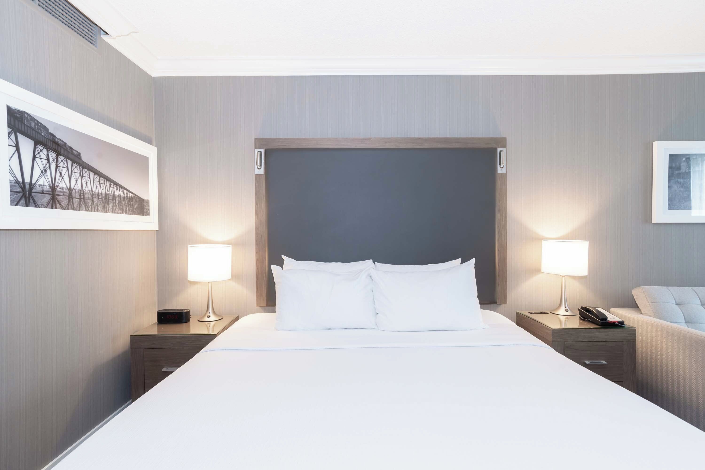 A hotel room with a large bed, two bedside tables with lamps, a chair, and a framed picture on the wall.