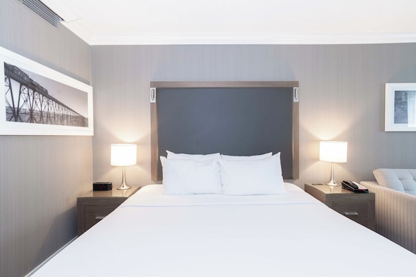 Habitación de hotel con una cama grande, dos mesitas de noche con lámparas, una silla y un cuadro en la pared.