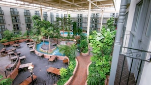 Un atrium interior con piscina central, rodeado de mesas y sillas, y abundante vegetación.
