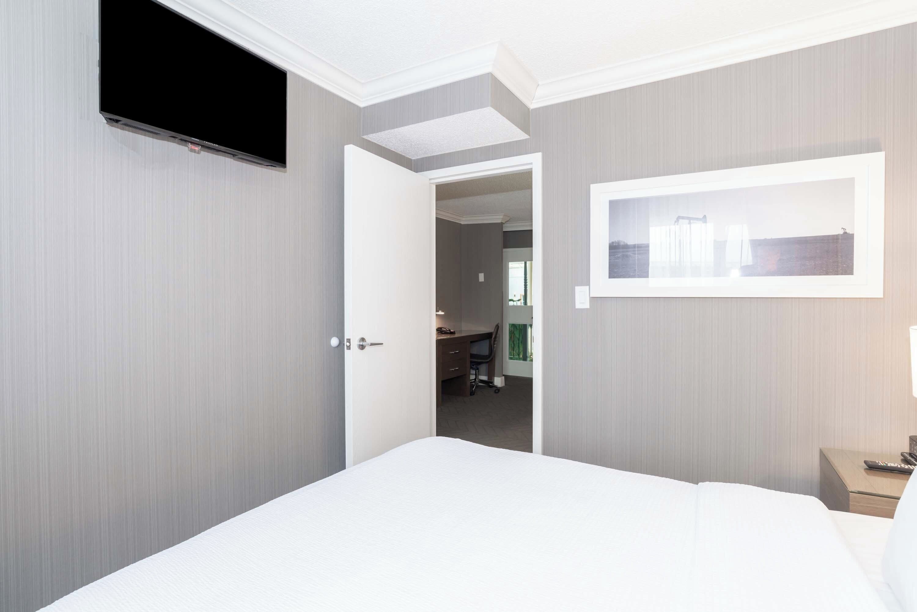 A hotel room with a bed, a TV mounted on the wall, a desk with a chair, and a framed picture on the wall.