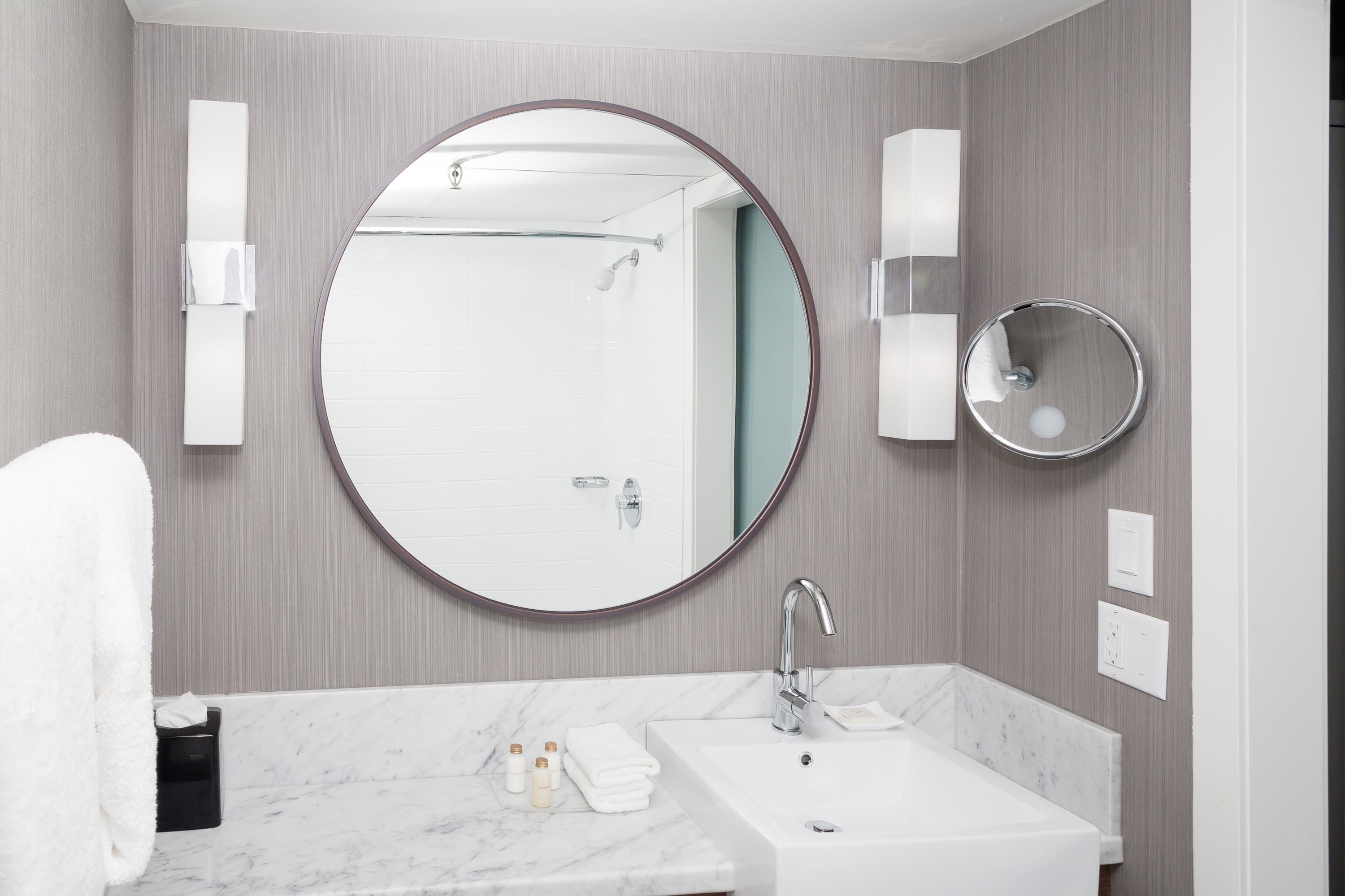 Une salle de bain moderne avec un grand miroir rond, un lavabo blanc et un porte-serviettes.