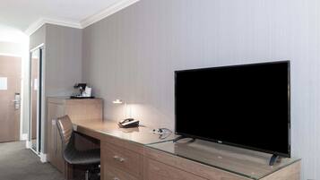 A modern hotel room with a glass desk, a flat-screen TV, a chair, and a desk lamp.