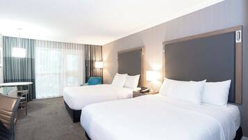 A hotel room with two beds, a desk, a chair, and a large window with curtains.