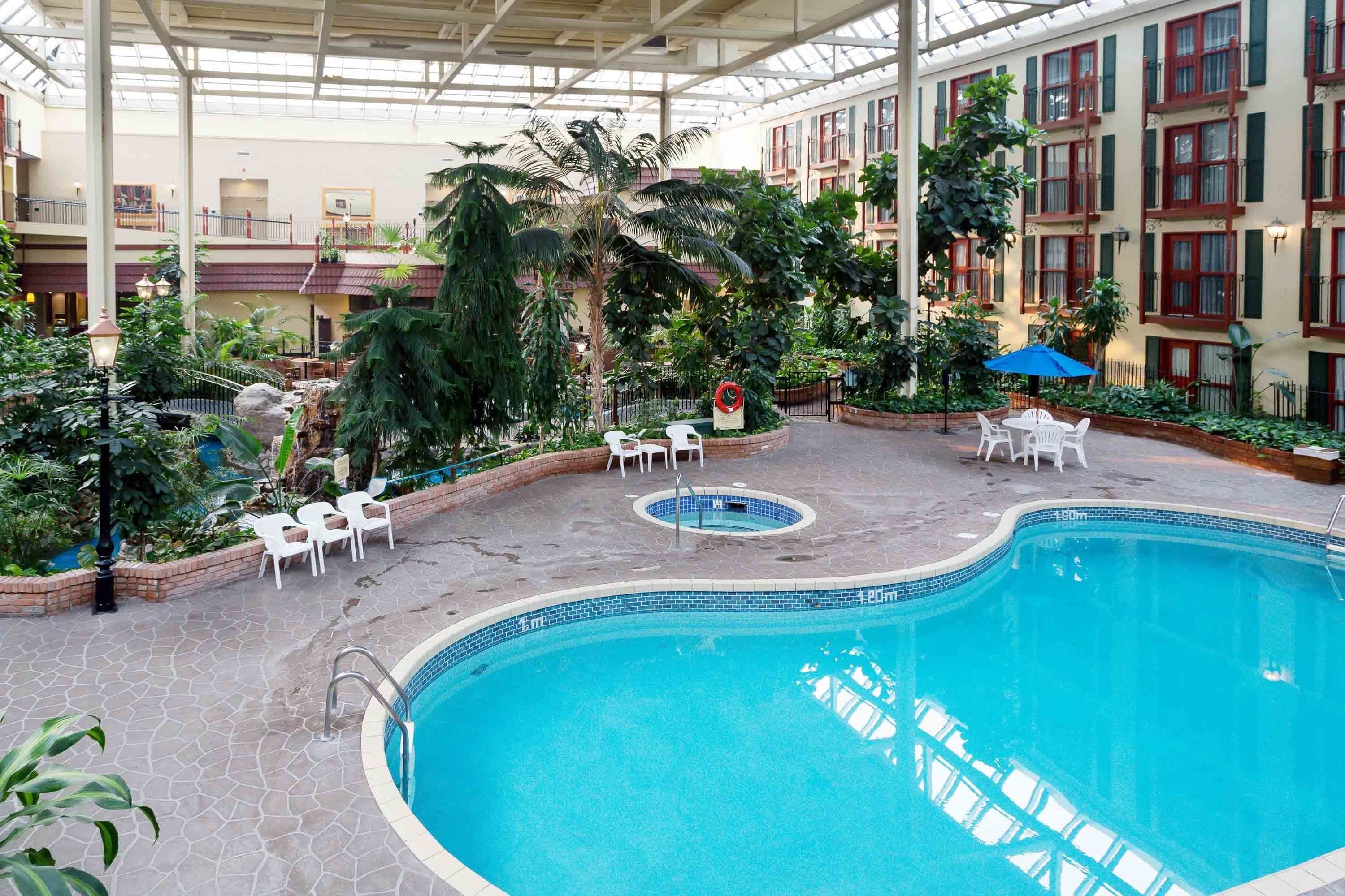 An indoor swimming pool with a tiled edge, surrounded by white chairs and a small circular hot tub.