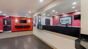 Un espace d’accueil avec un mur rouge, un comptoir noir et une pancarte indiquant « BIENVENUE ».