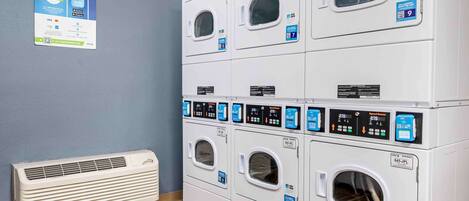 Een wasserette met meerdere wasmachines en drogers, een poster voor een app voor wasserettes, en een luchtverwarmer aan de muur.