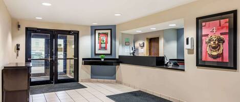 A hotel reception area with a reception desk, a framed picture on the wall, a door with a number, and a small plant on the counter.