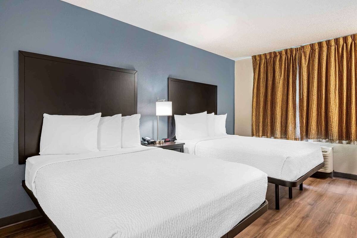 A hotel room with two beds, a nightstand with a lamp, and a window with curtains.
