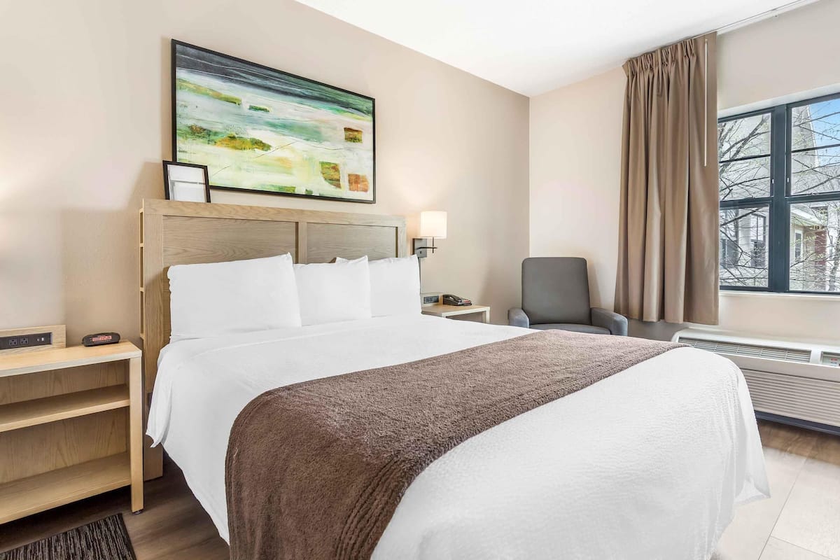 Una camera d'albergo con un letto grande, una scrivania, una sedia, una finestra con tende e un quadro appeso al muro.