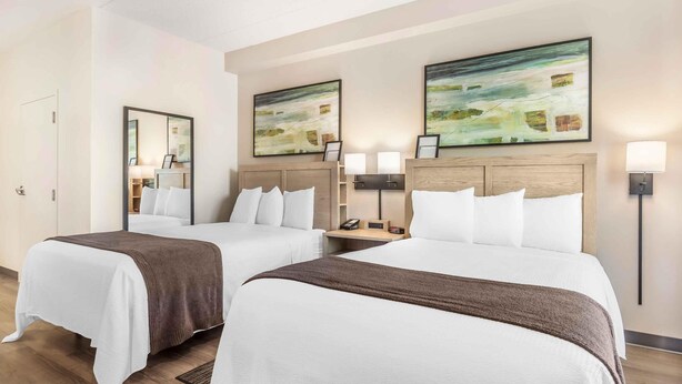 Habitación de hotel con dos camas, una mesita de noche con teléfono y lámpara, y obras de arte en las paredes.