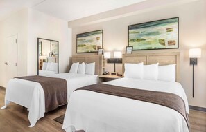 A hotel room with two beds, a nightstand with a phone and lamp, and artwork on the walls. - Extended Stay America Suites Long Island Melville (Melville)