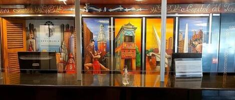 A reception area with a glass partition, a counter, and a mural depicting a cityscape with buildings and a bridge.