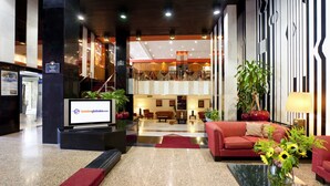 Eine Hotelhalle mit einer Rezeption, einem Fernseher, der die Hotelwebsite zeigt, einem roten Sofa, einem Couchtisch und einer großen Topfpflanze.