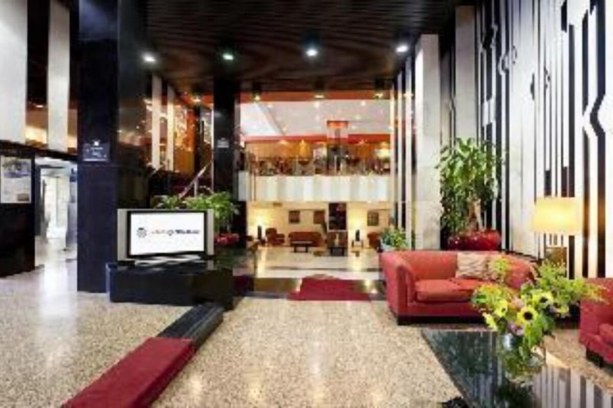 Un vestíbulo de hotel con una recepción, zona de estar y una escalera que sube a un nivel superior.