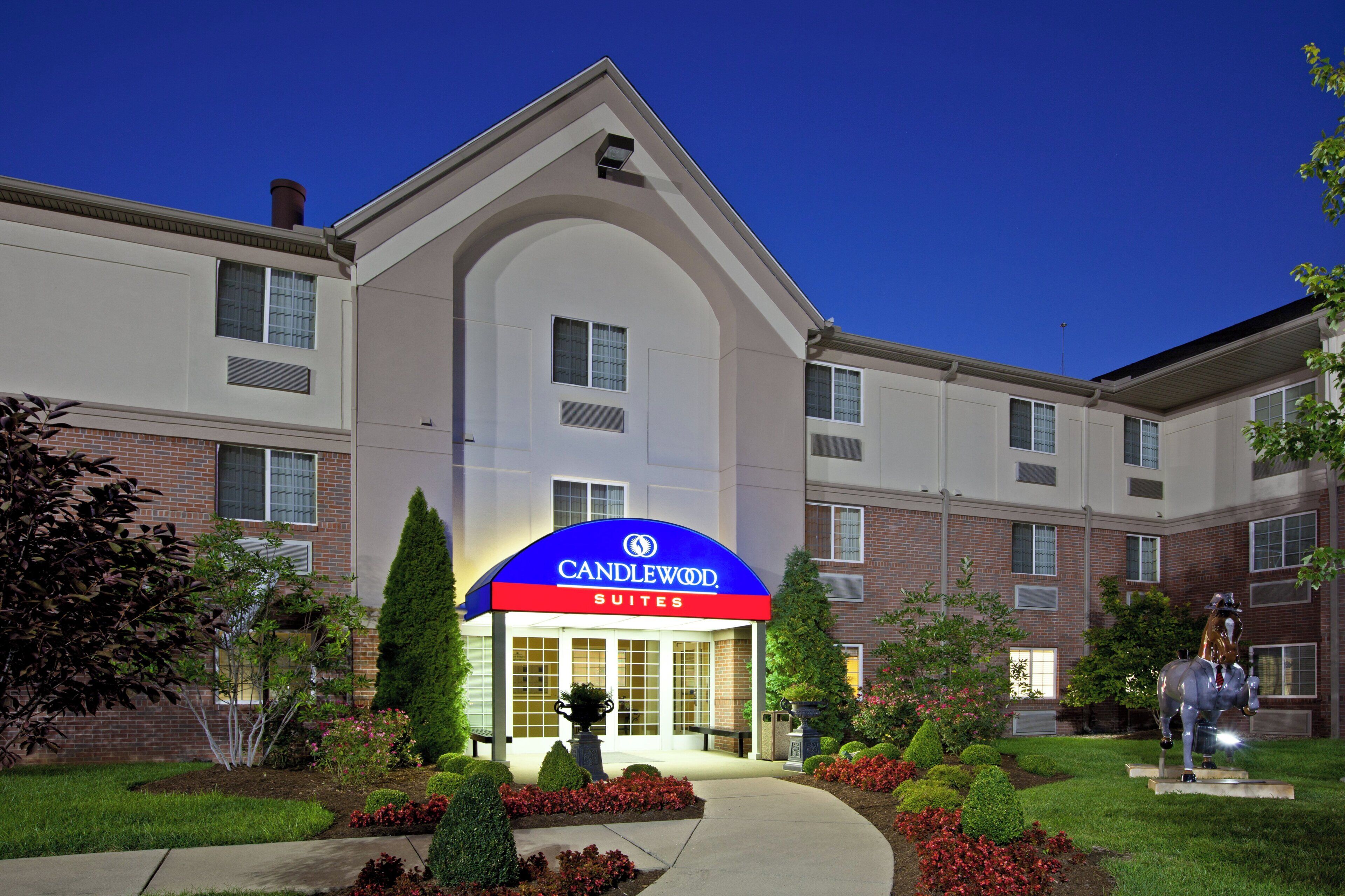 A hotel with a prominent blue and red sign, a brick facade, and a well-maintained garden with various plants and a statue.