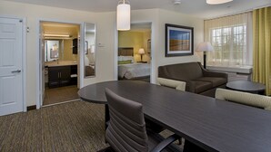 Habitación de hotel con mesa de comedor, dos sillas, sofá, una mesita redonda, lámpara, cama, baño y ventana con cortinas.