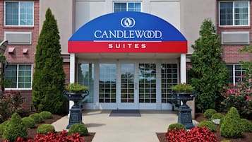 A hotel entrance with a sign reading 'CANDLEWOOD SUITES' and a symmetrical facade with windows and greenery.