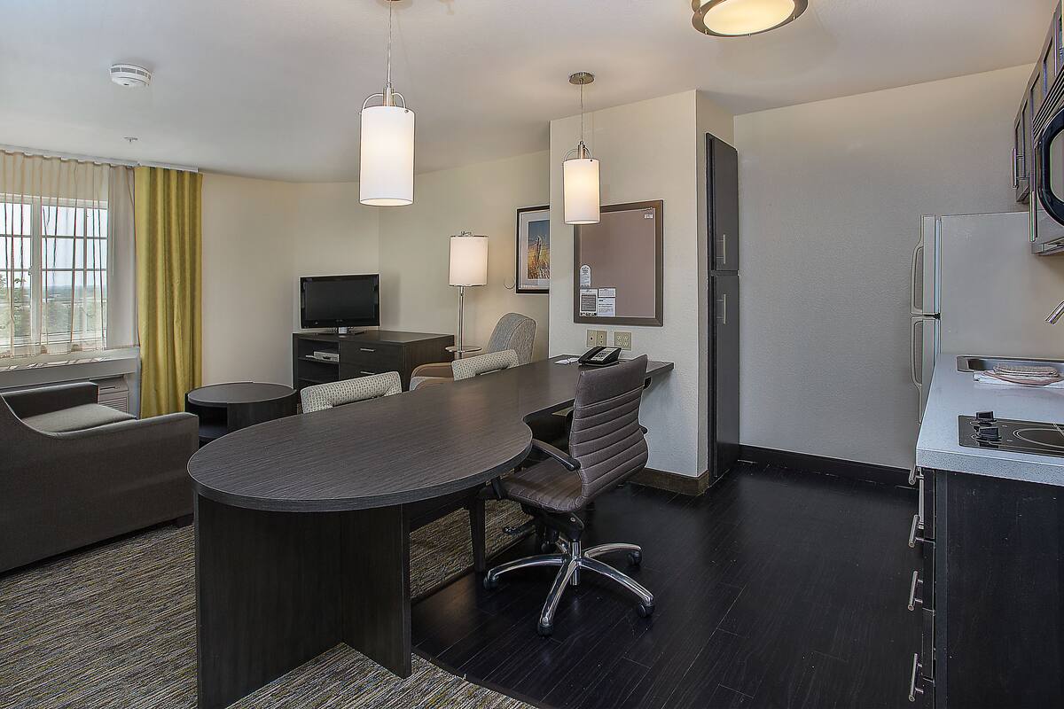 A modern hotel room with a dining area, a sofa, a TV, and a kitchen area with a microwave.