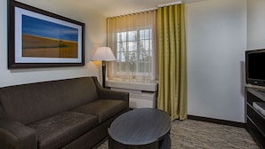 A hotel room with a sofa, a small table, a TV, a window with curtains, and a framed picture on the wall.