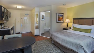 A hotel room with a bed, a desk, a chair, a bathroom, and a dining area.