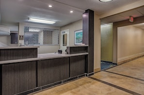 A reception area with a counter, a large mirror, a framed artwork, and a door with an exit sign. - Candlewood Suites Louisville Airport by IHG (Louisville)