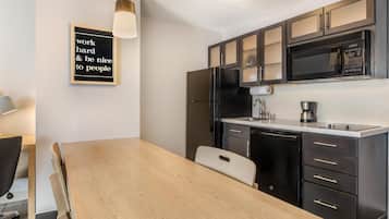 Une cuisine moderne avec une table à manger en bois, des meubles de rangement noirs et un four à micro-ondes.